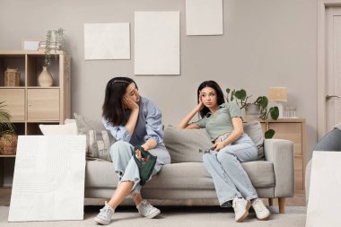 Evdeki tabloları asarken koltukta oturan yorgun genç kadınlar.