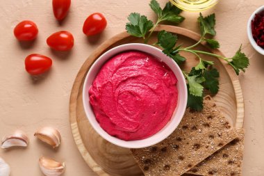 Bir kase lezzetli pancar humusu, domates, sarımsak, maydanoz ve bej arka planda kraker.