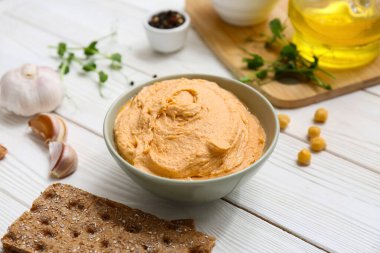 Beyaz ahşap arka planda sarımsaklı ve krakerli lezzetli humus kasesi.