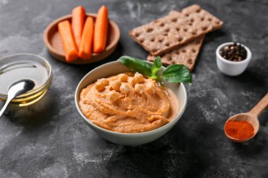 Siyah grunge arka planında havuç, nohut ve kraker olan lezzetli humus kasesi.