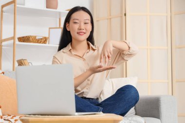 Evdeki video konuşmasında işaret dili kullanan Asyalı kadın.