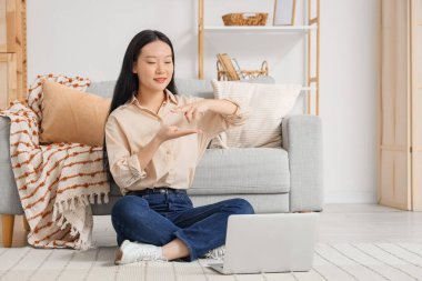 Evdeki video konuşmasında işaret dili kullanan Asyalı kadın.