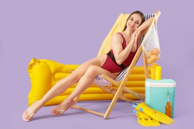 Güverte sandalyesinde oturan güzel bir kadın. Plaj aksesuarları ve leylak arka planda.