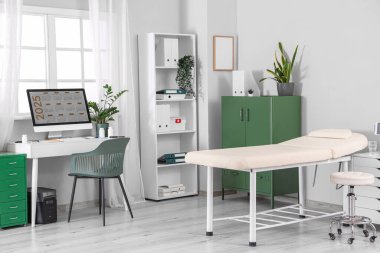 Doktorun çalışma yeri, raf ünitesi ve kanepesi olan sağlık bürosu.