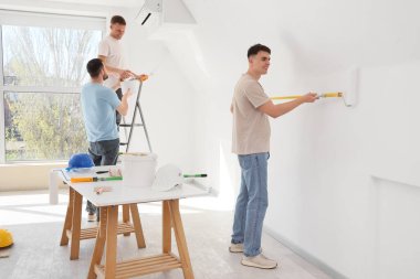 Genç adamlar odada duvar boyuyor.