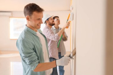 Bir grup genç adam odada duvar boyuyor.