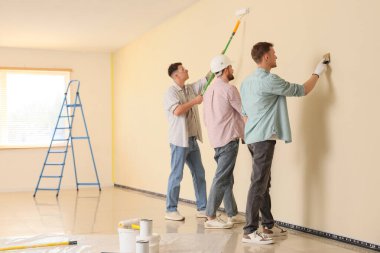 Bir grup genç adam odada duvar boyuyor.