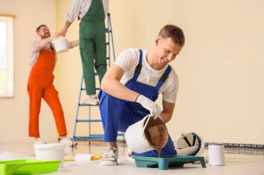 Erkek dekoratör odada tepsiye boya döküyor.