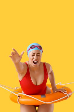 Sarı arka planda halka şamandırası olan korkmuş Afro-Amerikan yüzücü kadın.