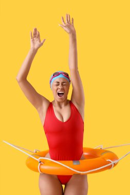 Sarı arka planda halka şamandırası olan korkmuş Afro-Amerikan yüzücü kadın.