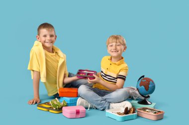 Beslenme çantalı küçük çocuklar mavi arka planda oturuyorlar.