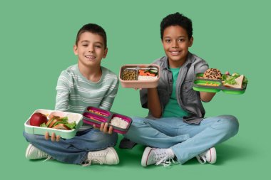 Beslenme çantaları yeşil arka planda oturan sevimli çocuklar.