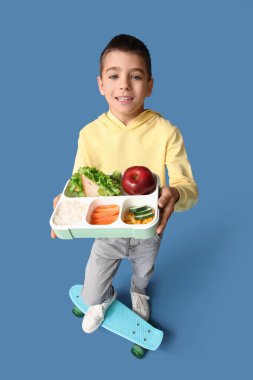 Sefertası ve mavi arka planda kaykayı olan küçük bir çocuk.