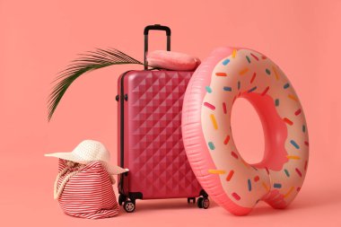 Pembe arka planda plaj aksesuarları, bavul ve palmiye yaprağı.