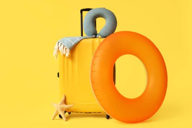 Seyahat yastığı, havlu, şişirilebilir yüzük ve sarı arka planda deniz yıldızı olan şık bir bavul.