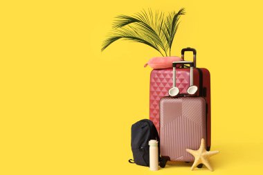 Şık bavullar, sırt çantası, seyahat yastığı, hindistan cevizi ve sarı arka planda palmiye yaprakları.