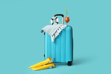 Plaj aksesuarlarıyla dolu bavul ve renkli arka planda bir bardak kokteyl.