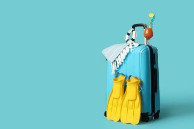 Plaj aksesuarlarıyla dolu bavul ve renkli arka planda bir bardak kokteyl.