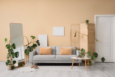 Masa, kanepe ve evin çiçekleri odanın içindeki bej duvarın yanında.