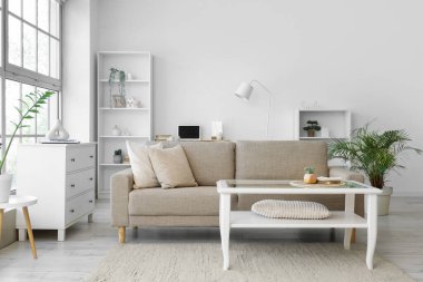 Oturma odasının içinde yumuşak kanepe, masa ve raf üniteleri.