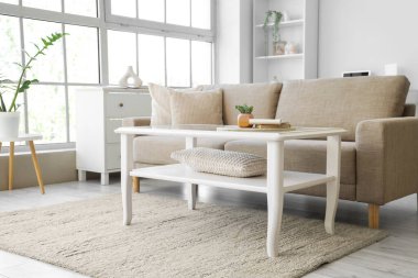 Oturma odasının içinde yumuşak kanepe, masa ve pencere var.