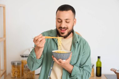 Genç adam mutfakta lezzetli ramen yiyor.