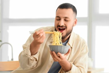 Genç adam mutfakta lezzetli ramen yiyor.