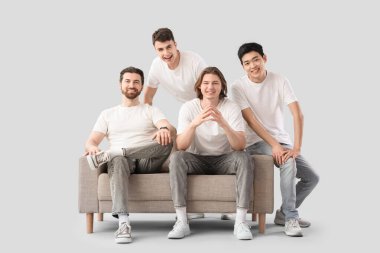 Beyaz tişörtlü ve arka planda kanepesi olan bir grup genç adam.