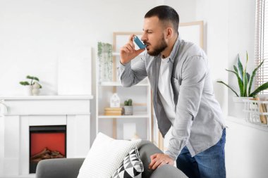 Genç adam evde astım spreyi kullanıyor.