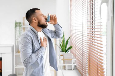 Astım krizi geçiren genç bir adam evde astım spreyi kullanıyor.
