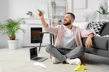 Ofiste kağıttan uçakla oturan genç bir adam.