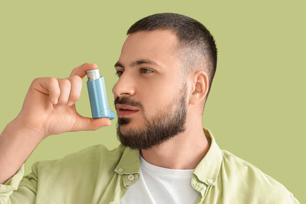 Молодой человек использует ингалятор на зеленом фоне