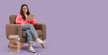 Yığınla kitabı olan genç bir kadın, eflatun arka planda koltukta oturuyor ve mesaj için yeri var.