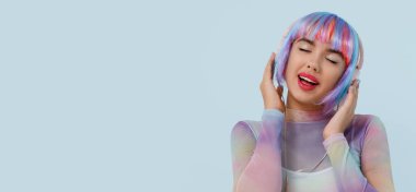 Renkli peruklu güzel bir genç kadının portresi açık mavi arka planda müzik dinliyor ve metin için yer var.