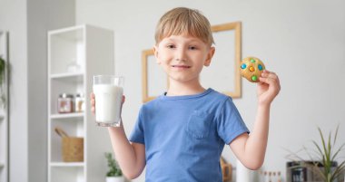 Bir bardak süt ve kurabiyeyle mutfak tezgahında oturan küçük çocuk.