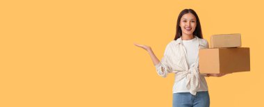 Sarı arka planda bir şey gösteren paketleri olan güzel bir genç kadın.