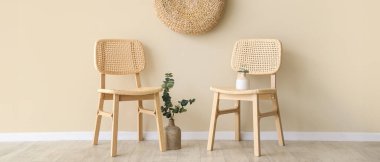 İçinde okaliptüs dalları ve bej duvarın yanında puf bulunan rahat ahşap sandalyeler.