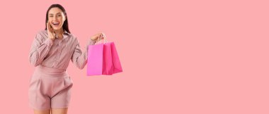 Pembe arka planda alışveriş torbaları olan şaşırmış genç bir kadın.