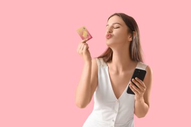 Pembe arka planda kredi kartı ve cep telefonu olan genç bir kadın.
