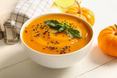 Bir kase lezzetli kabak kremalı çorba, tohumlu ve fesleğenli beyaz ahşap masa.