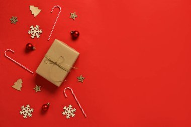 Kırmızı arka planda Noel süsleri ve şeker kamışları olan hediye kutusu.