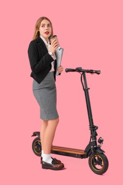 Paket servis bardağı, dosya ve pembe arka planda scooter 'ı olan genç bir iş kadını portresi.