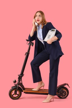 Tekme scooterlı genç bir iş kadınının portresi pembe arka planda telefonla konuşuyor.