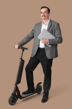 Bej arka planda scooter ve laptop kullanan genç iş adamının portresi