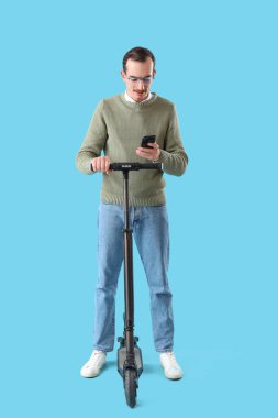 Mavi arka planda cep telefonu ve scooter 'ı olan genç adam.