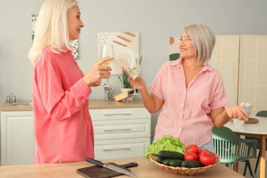 Olgun bayan arkadaşlar mutfakta şarap içiyor.