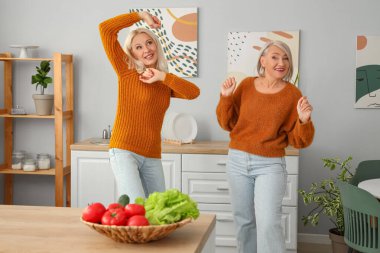 Olgun bayan arkadaşlar mutfakta dans ediyor.