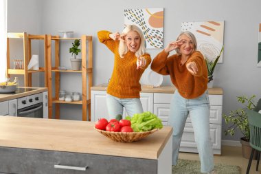 Olgun bayan arkadaşlar mutfakta dans ediyor.