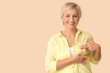 Güzel olgun bir kadın bej arka planda göğüslerini kontrol ediyor. Kanser farkındalığı kavramı