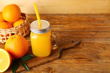 Mason kavanozu taze portakal suyu ve ahşap arka planda meyveler.